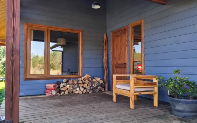 Terraza de madera con sillón, leña y acceso a la casa en Casa Altos de Molco
